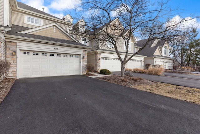 view of home's exterior featuring aphalt driveway, stone siding, roof with shingles, and a garage