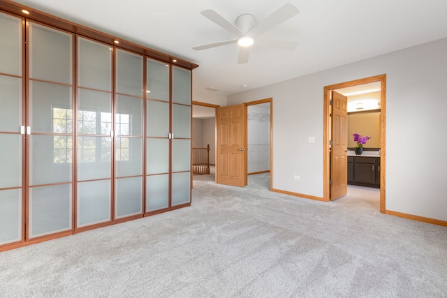 unfurnished bedroom featuring a spacious closet, baseboards, ensuite bathroom, and light colored carpet