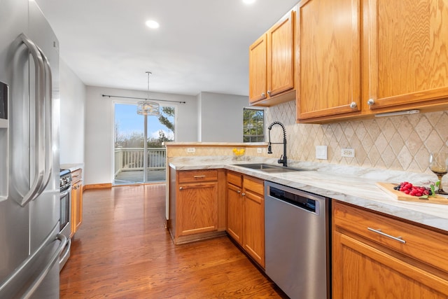 kitchen featuring a peninsula, wood finished floors, a sink, appliances with stainless steel finishes, and tasteful backsplash