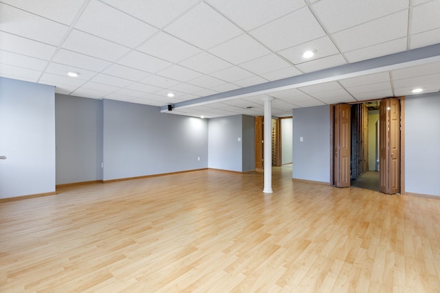 finished basement featuring light wood finished floors, a drop ceiling, and baseboards