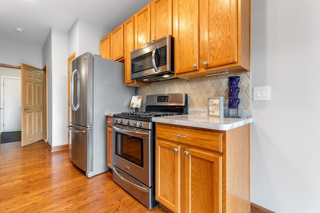 kitchen with tasteful backsplash, baseboards, stainless steel appliances, light countertops, and light wood-style floors