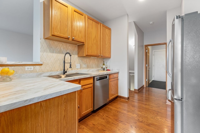 kitchen with stainless steel appliances, light countertops, decorative backsplash, light wood-style floors, and a sink