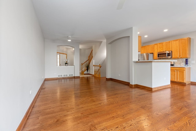 unfurnished living room featuring a ceiling fan, stairway, arched walkways, and wood finished floors