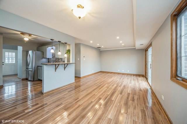 kitchen featuring light wood-type flooring, freestanding refrigerator, decorative backsplash, and a breakfast bar area