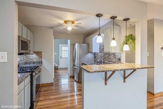 kitchen with stainless steel appliances, a breakfast bar, a peninsula, light wood-style floors, and light stone countertops