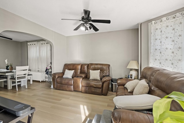 living area with ceiling fan, arched walkways, radiator, and wood finished floors