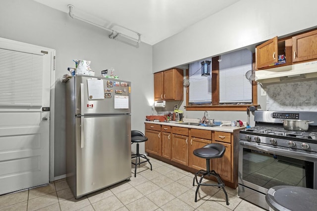 kitchen with a sink, stainless steel appliances, light countertops, under cabinet range hood, and brown cabinets