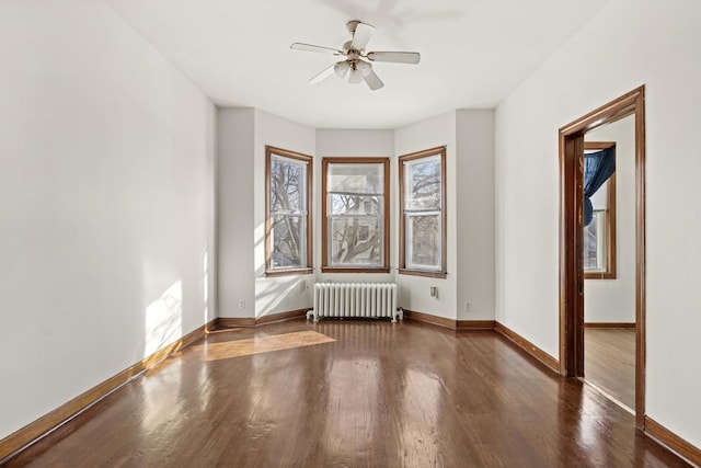 spare room featuring a ceiling fan, radiator, wood finished floors, and baseboards