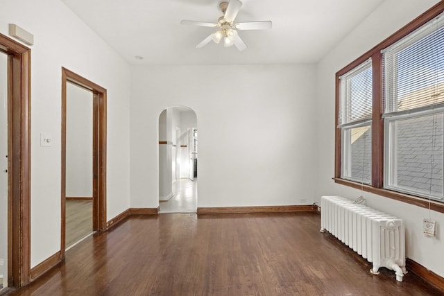 spare room featuring radiator, dark wood-style floors, arched walkways, and baseboards