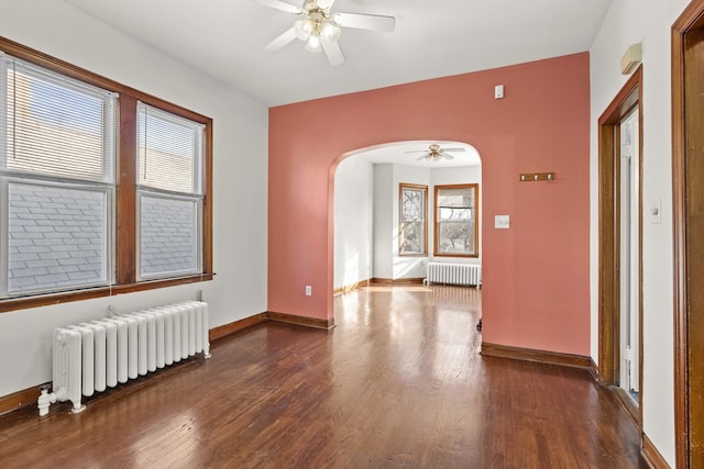 empty room with arched walkways, radiator heating unit, a ceiling fan, and wood finished floors