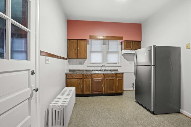 kitchen featuring radiator, brown cabinetry, freestanding refrigerator, a sink, and dark countertops