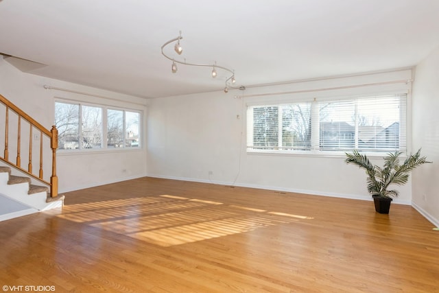 empty room with light wood-type flooring, baseboards, and stairs