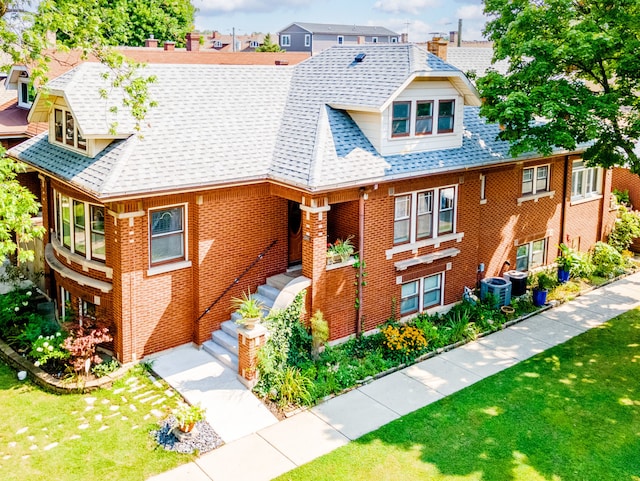 view of front of property featuring central air condition unit, a shingled roof, a front yard, and brick siding