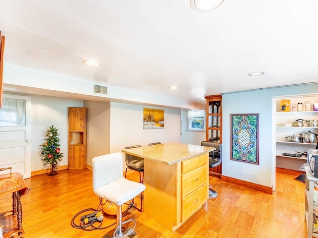 kitchen featuring light wood finished floors, baseboards, visible vents, a kitchen island, and a breakfast bar