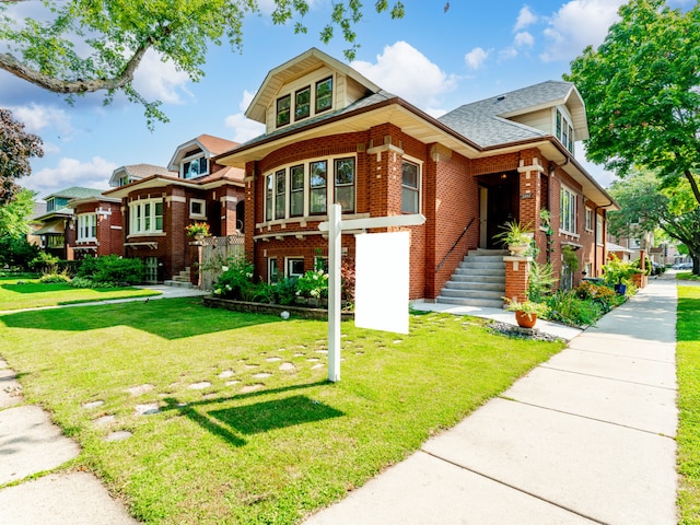 view of front of home featuring roof with shingles, a front yard, and brick siding