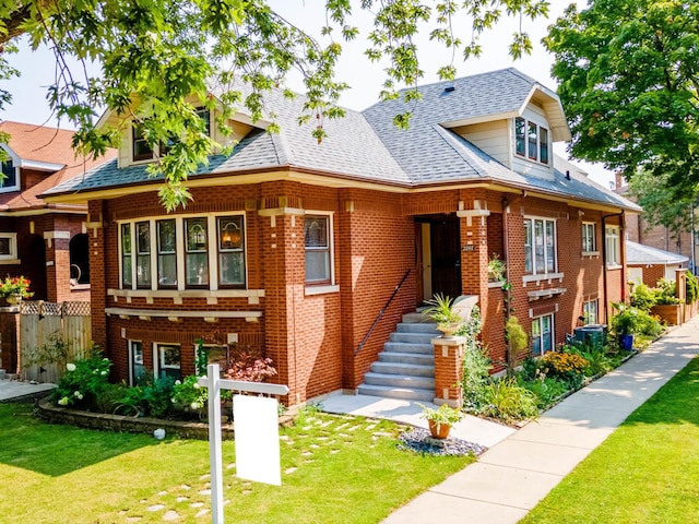 view of front of house featuring a shingled roof, fence, a front lawn, and brick siding