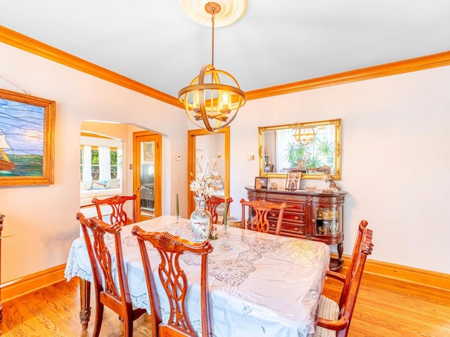 dining room featuring baseboards, arched walkways, wood finished floors, crown molding, and a notable chandelier