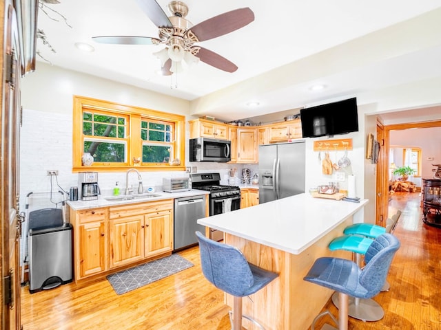 kitchen with a breakfast bar, a sink, light countertops, appliances with stainless steel finishes, and light wood finished floors