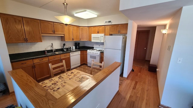 kitchen with tasteful backsplash, visible vents, brown cabinetry, a sink, and white appliances