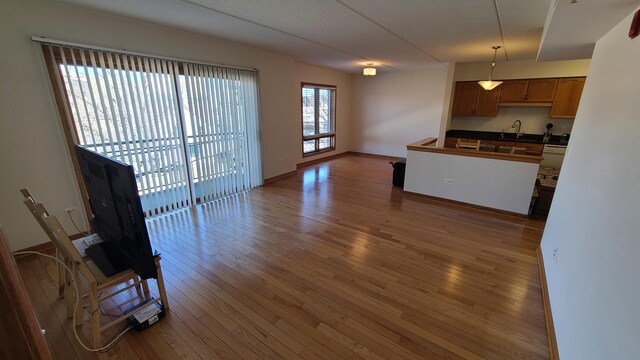 kitchen with baseboards, dark countertops, wood-type flooring, hanging light fixtures, and a sink