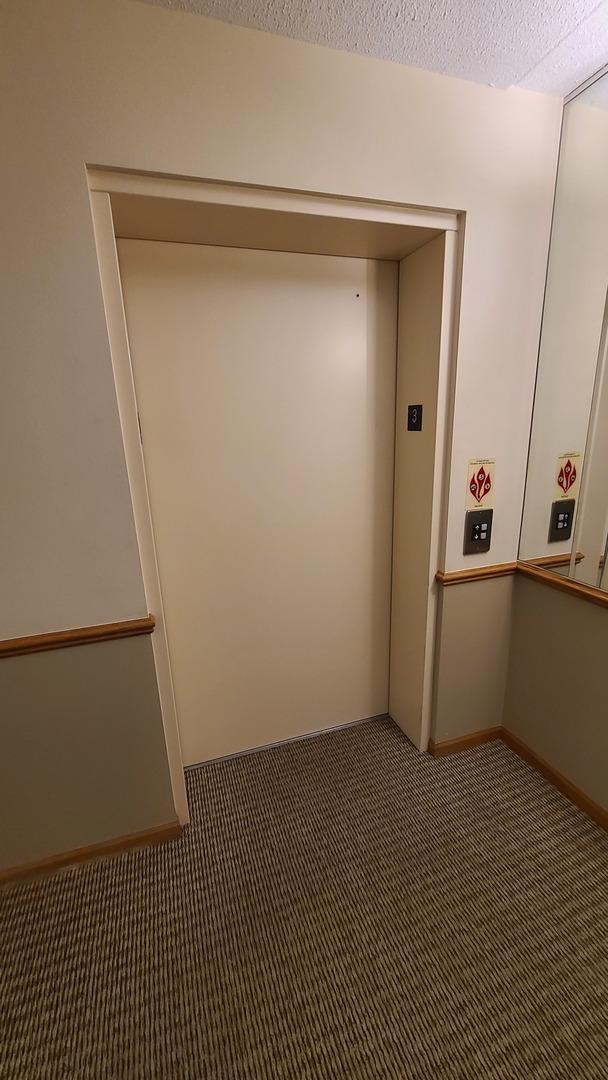 corridor featuring elevator, a textured ceiling, baseboards, and carpet flooring