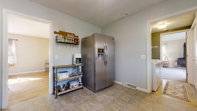 kitchen with visible vents, stainless steel refrigerator with ice dispenser, separate washer and dryer, baseboards, and a wood stove