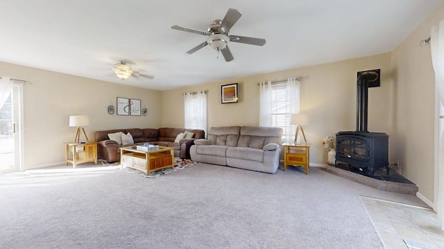 carpeted living room featuring baseboards, a wood stove, and ceiling fan