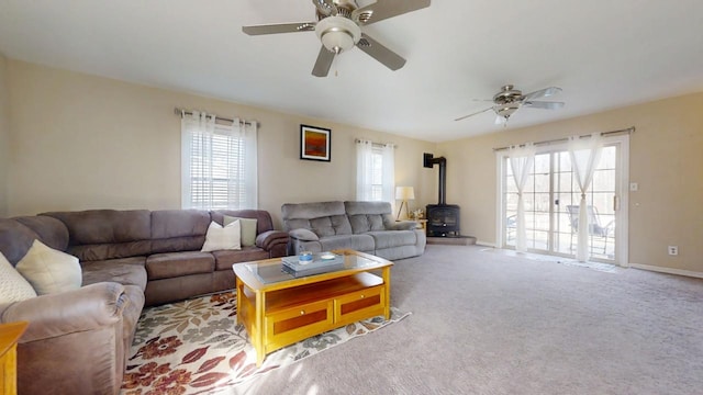 living area featuring a wealth of natural light, carpet flooring, baseboards, and a wood stove