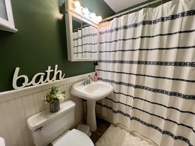 full bath with curtained shower, a textured ceiling, toilet, and wainscoting