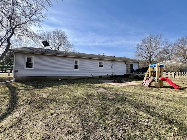 rear view of house with a lawn, a playground, and fence