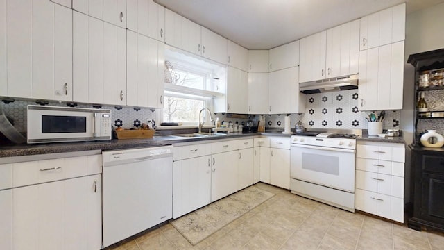 kitchen with under cabinet range hood, a sink, backsplash, dark countertops, and white appliances