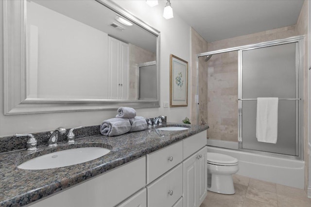 bathroom featuring combined bath / shower with glass door, double vanity, a sink, and toilet