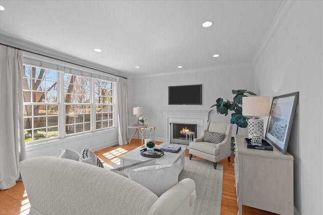 living room featuring recessed lighting, light wood-style flooring, crown molding, and a warm lit fireplace