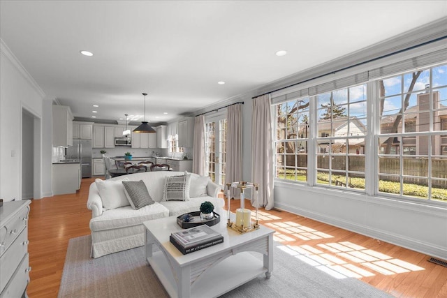 living area with ornamental molding, light wood finished floors, and plenty of natural light