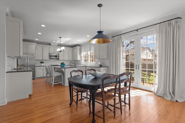 dining room featuring ornamental molding, french doors, light wood-type flooring, and an inviting chandelier