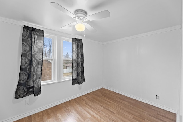 empty room with crown molding, wood finished floors, a ceiling fan, and baseboards