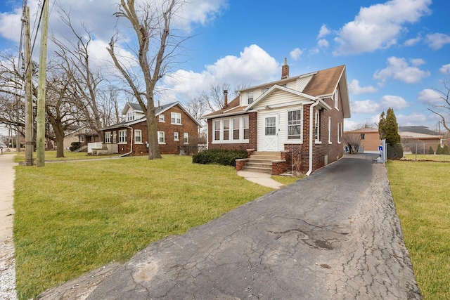 bungalow-style house featuring aphalt driveway, brick siding, a chimney, a front yard, and fence