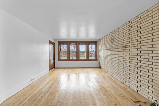 empty room featuring baseboards, brick wall, visible vents, and light wood-style floors