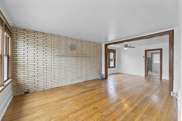 empty room featuring ceiling fan, brick wall, baseboards, and wood-type flooring