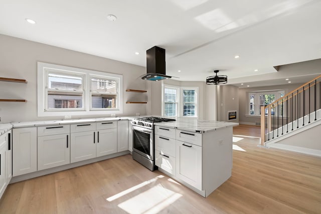 kitchen featuring gas range, island range hood, open shelves, and light wood-style floors