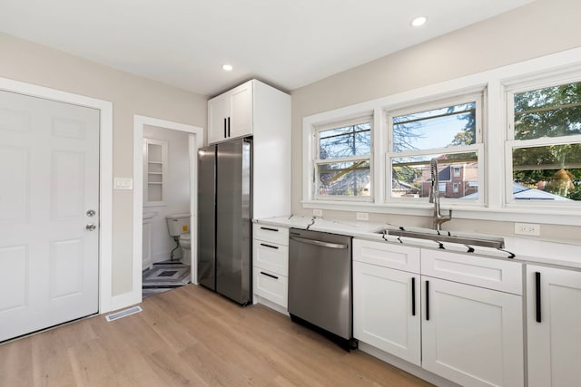 kitchen with visible vents, white cabinets, stainless steel appliances, light wood-type flooring, and a sink