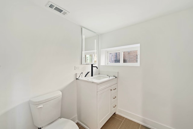 bathroom featuring toilet, vanity, visible vents, and baseboards