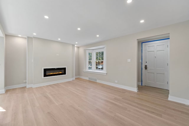 unfurnished living room featuring light wood-style floors, recessed lighting, visible vents, and a glass covered fireplace