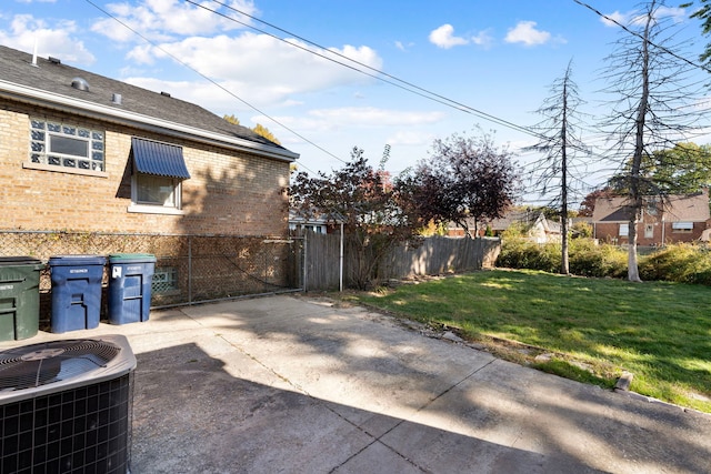 exterior space with central air condition unit, brick siding, fence, a yard, and a gate