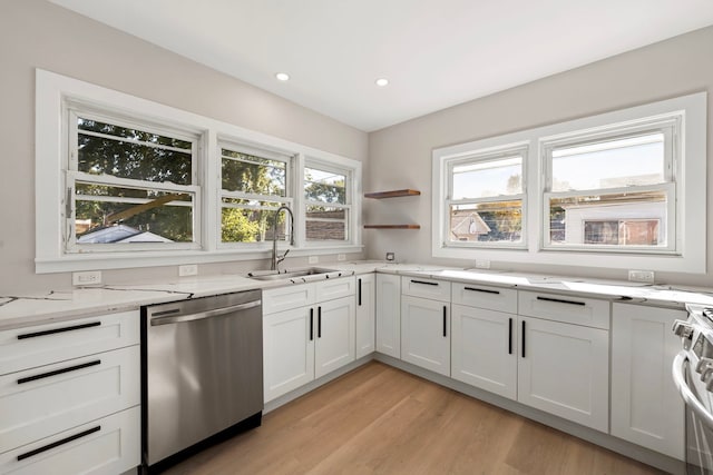 kitchen featuring light stone counters, light wood-style flooring, appliances with stainless steel finishes, white cabinets, and a sink