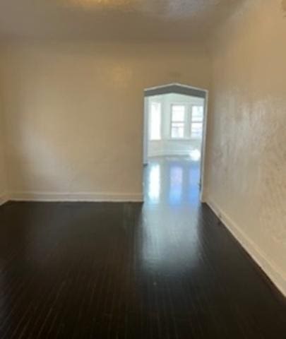 spare room featuring baseboards and dark wood-type flooring