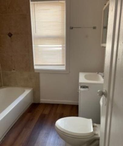 full bathroom with baseboards, toilet, wood finished floors, vanity, and a bath