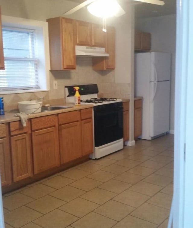 kitchen with under cabinet range hood, range with gas stovetop, light countertops, backsplash, and freestanding refrigerator