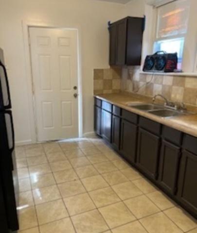 kitchen featuring light tile patterned floors, light countertops, backsplash, freestanding refrigerator, and a sink