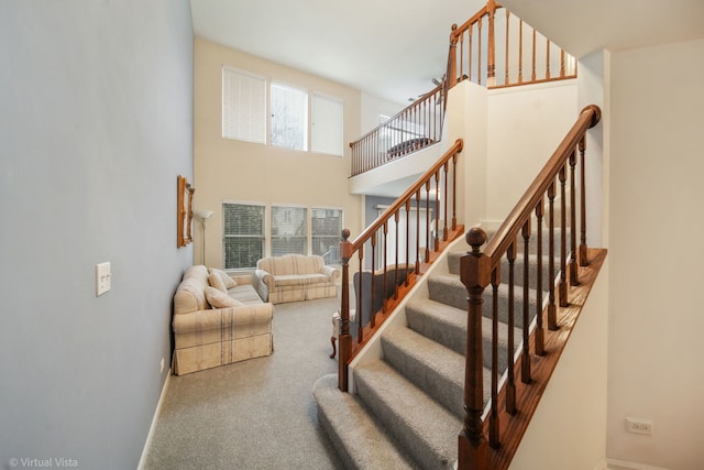 staircase with a towering ceiling, baseboards, and carpet flooring